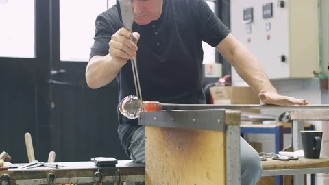 Man blowing and shaping hot glass on blowpipe in workshop Video stock 107888779