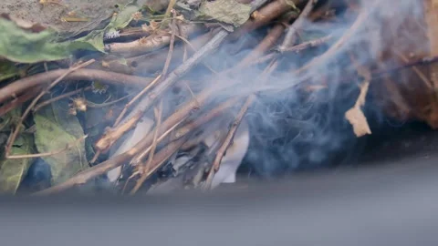 Man Blowing on Small Fire to Ignite Paper and Thin Wooden Twigs in Outdoor Fire Stock Footage 344813875