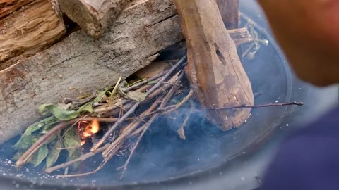 Man Blowing on Small Fire to Ignite Paper and Thin Wooden Twigs in Outdoor Fire Stock Footage 344814991