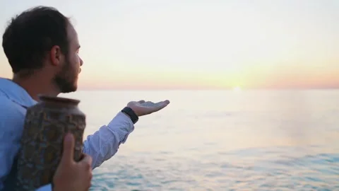 A man blows ashes from the palm of his hand with ashes from a cremation urn, the Stock Footage 247337745
