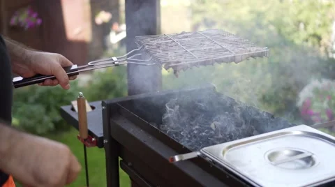 Man blows coals in brazier, swinging a red plastic cutting board Stock Footage 68675446