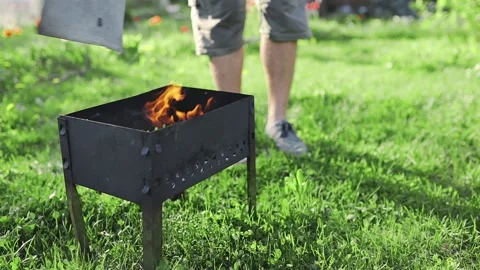 Man blows to the coals to rise the flame and heat in his grill, BBQ at the Stock Footage 89628188