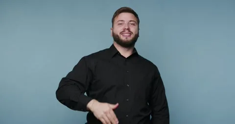 Man blows a kiss while standing against a blue background in a casual setting 스톡 동영상 326798563