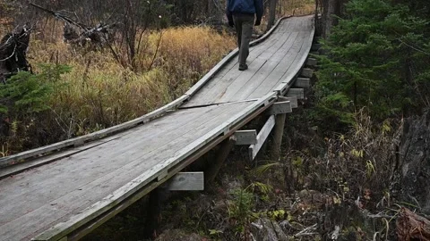 A man in blue coat and black gloves walks along a dilapidated wooden walkway Stock Footage 143786336