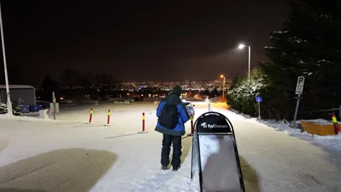 Man in blue coat walking into snowy Fjellheisen car park in Tromso, Norway Stock Footage 301551876