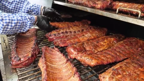 Man in Blue Gingham Shirt Adjusting Slabs of Barbecue Pork Ribs on a Large Smoke Stock Footage 338212506