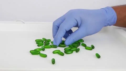 Man with blue glove pinking up one green tablet from bunch of green tablets Stockbeeldmateriaal 147699875