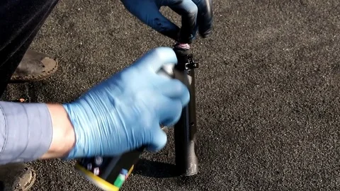 A man in blue gloves paints a small metal detail with black paint from a can Stock Footage 89434633