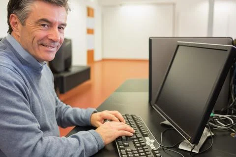 Man in blue-gray sweater typing on full keyboard at training room with monitor, Stock Photos
