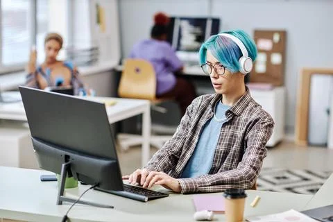 Man with blue hair using computer in office Stock-Fotos