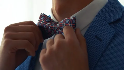 A man in a blue jacket and white shirt corrects blue and red bow tie. Video stock 131095710