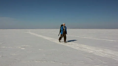 Man in a blue jacket with a backpack is skiing on the ice of the frozen river Stock Footage 87784315