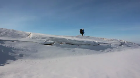 Man in a blue jacket with a backpack is skiing on the ice of the frozen river Stock Footage 87784322