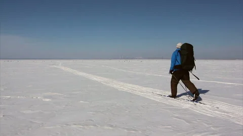 Man in a blue jacket with a backpack is skiing on the ice of the frozen river Stock Footage 87784355