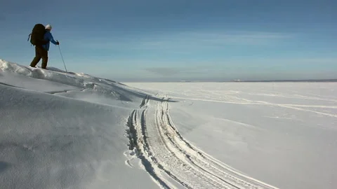 Man in a blue jacket with a backpack is skiing on the ice of the frozen river Stock Footage 87784390
