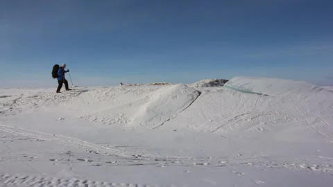 Man in a blue jacket with a backpack is skiing on the ice of the frozen river Stock Footage 87784424