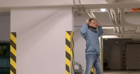 A man in a blue jacket dances energetically in a parking garage Stock Footage 313564285