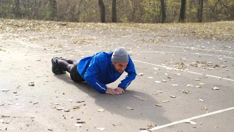 Man in blue jacket doing push-ups outdoors on autumn park pavement, training Stock Footage 315584137