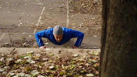 Man in blue jacket doing push-ups against concrete step in autumn park, outdoor Stock Footage 315584296