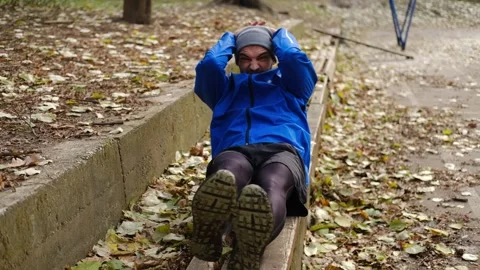 Man in blue jacket doing sit-ups on bench in autumn park, exercising abs during Stock Footage 315584695