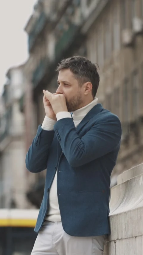 A man in a blue jacket plays the harmonica on the street looking up Vidéo 328343252