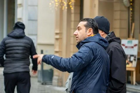 Man in blue jacket points direction to companions on city street. Istanbul Stock Photos