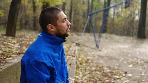 Man in blue jacket resting on bench in park, drinking water after training on Stock Footage 315584842