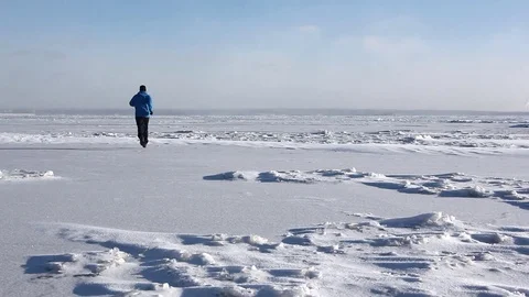 Man in a blue jacket running across the ice of a frozen river Stock Footage 82887720