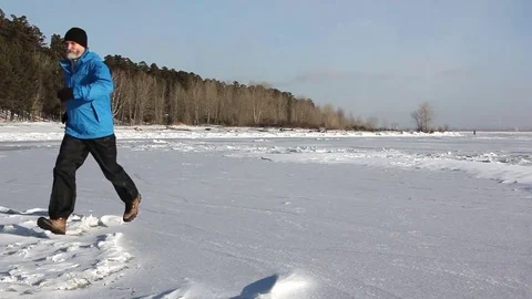Man in a blue jacket running across the ice of a frozen river Stock Footage 82887727