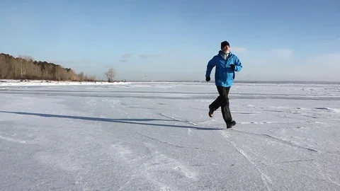 Man in a blue jacket running across the ice of a frozen river Stock Footage 82887735