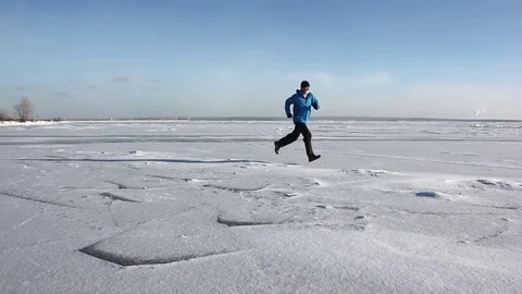 Man in a blue jacket running across the ice of a frozen river Stock Footage 82887754