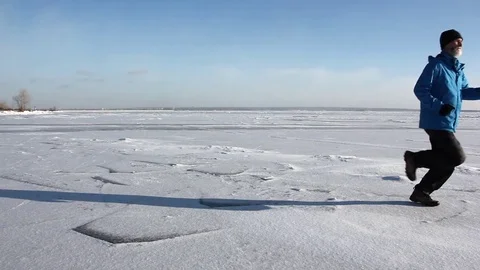 Man in a blue jacket running across the ice of a frozen river Stock Footage 82887760