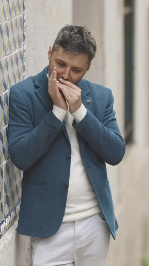 A man in a blue jacket stands against the wall and plays the harmonica in the Vidéo 328343259