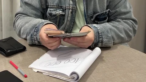 Man in blue jeans denim jacket at table counts cash money Vídeos de archivo 329666917