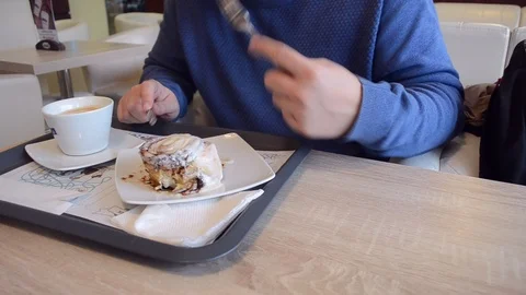 A man in a blue jumper drinks and eats coffee with cake in a cafe at a table Stock Footage 123832760