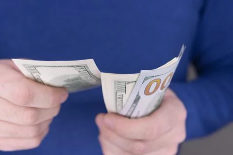 A man in a blue jumper holds a stack of 100 dollars in his hands Stock Photos