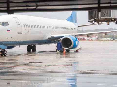 A man in a blue raincoat approaches the engine of an airliner on the runway on a Stock Photos
