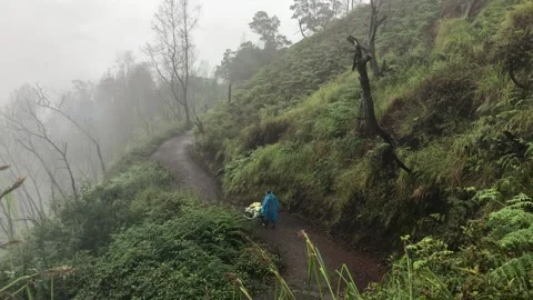 A man in a blue raincoat moves down the slope Stock Footage 169774081