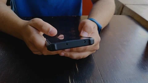 Man with blue shirt browsing on a touch screen cellphone, sitting at table Stock Footage 108440315