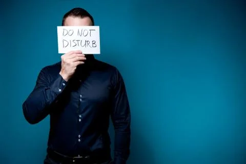 A man in a blue shirt covers his face with a do not disturb sign Stock Photos