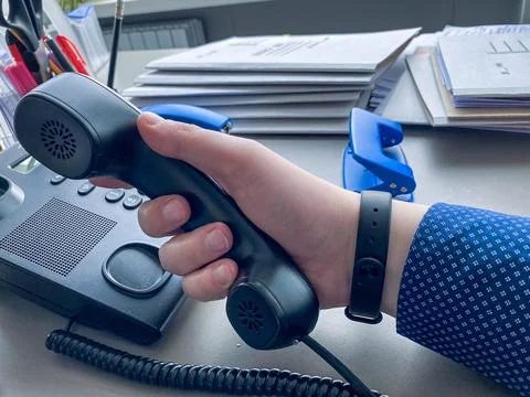 A man in a blue shirt with a pattern picks up a black phone to make a call. o 写真素材