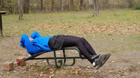 Man in blue sports jacket doing sit-ups on outdoor bench in autumn park Stock Footage 316821973