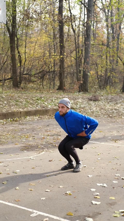 Man in blue sports jacket doing squats outdoors in autumn park, exercising for Stock Footage 316822938