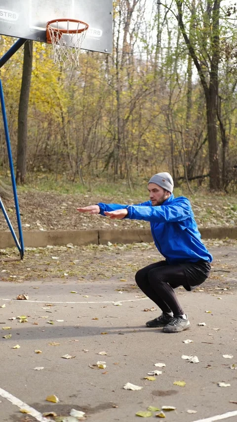Man in blue sports jacket doing squats with arms extended on basketball court in Stock Footage 316823450