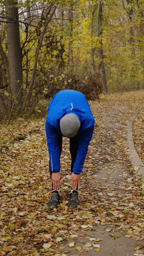 Man in blue sports jacket doing warm-up in autumn forest park before outdoor Stock Footage 316824878
