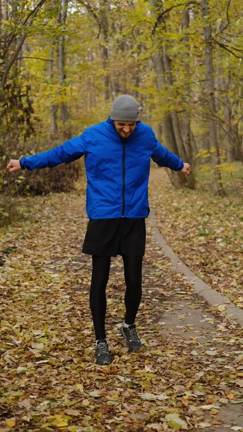 Man in blue sports jacket doing warm-up in autumn forest park before outdoor Stock Footage 316825987