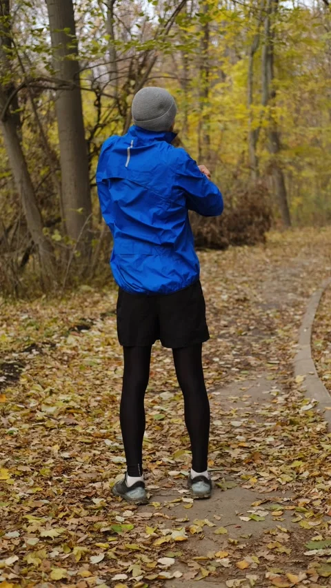 Man in blue sports jacket doing warm-up in autumn forest park, standing with Stock Footage 316826129