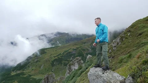 The man in blue stands on the edge of the cliff and radiates victory, hands up Stock Footage 233175723