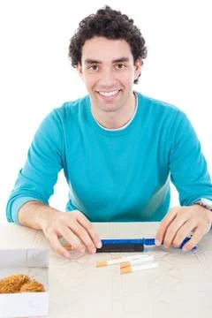 Man in blue sweater making cigarettes with device for cigar and dry tobacco o Stock Photos