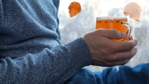 Man in a blue sweater is sitting by the window with a mug of sea buckthorn tea. Stock Footage 127022580